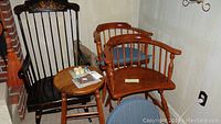 Photo showing two wooden chairs with blue cushions, black Hitchcock style rocking chair with floral decoration, and round wooden stool.
