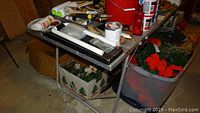 Photo showing metal folding table with painting supplies including paint brushes, paint rollers, paint containers, and a paint tray.