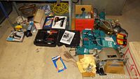 Wide view of all power tools including boxed items, Makita sanders, drill, blades, and accessories arranged on floor and shelving.