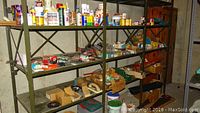 Photo of metal shelving holding multiple small boxes and containers with assorted nails, screws, and hardware supplies stored on three shelves.