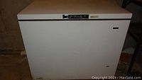 White Kenmore chest freezer with top lid closed, visible wear and scuff marks on exterior.