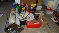 Lot contents on floor of garage showing tow winch, tool boxes, jumper cables, plastic sheets, car care liquids, and tools.
