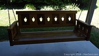 Wooden porch swing with decorative acorn cutout backrest, shown outdoors on concrete surface.