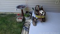 Photo showing vintage rusty metal wagon with wooden handle, rusty metal bird bath, small garden pots, and shepherd hooks.