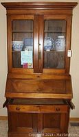 Front view of the two-piece antique walnut secretary desk with glass bookcase top displaying china inside.