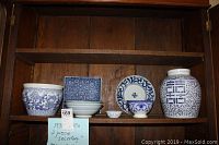 Full view of shelf with two vases, four bowls, and two plates in blue and white ceramic designs showing a mix of oriental and European styles.