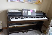 Full view of Roland Midi Piano 5600 digital keyboard with music stand and pedals, placed against wall.