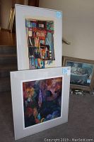 Two framed paintings leaning against a wall indoors