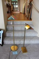 View showing both brass apothecary lamps on carpeted stairs, one taller with round base and one shorter with square base.