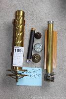 Photo showing two brass kaleidoscopes, multiple small accessories, and a small brass hand bell all arranged on carpet.