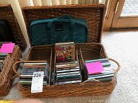 Wicker basket with stacks of CDs and green carrying case inside.