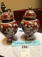 Front view of two matching cloisonne temple jars with red base and white floral patterns, brass finial lids visible