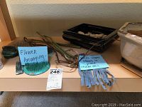 Photo of green and metal flower frogs, spiked bases, natural floral stems, and black rectangular glazed vase with stones inside