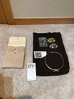Overview of beige jewelry pouch, black display cloth, collar necklace, two brooches and information card