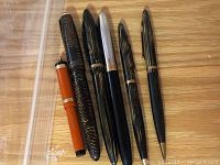 Six vintage fountain pens arranged in a row on a wooden surface, showing different colors and designs.