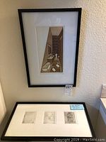 Two framed etchings displayed on a wall and shelf, one vertical of a bathroom scene and another horizontal frame with three smaller etchings.