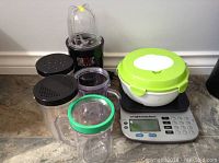 Magic Bullet blender with four clear blending cups and lids, Weight Watchers digital scale with white storage bowl with green lid on top.