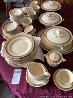 Full view of all dishes and serveware including stacked plates, cups and saucers, lidded serving dishes and gravy boat displayed on table.