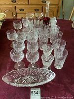 Photo showing entire assortment of crystal glassware including various styles of stemware, highball glasses, decanter, and serving pieces arranged on a table.