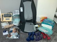 Photo shows multiple health-related items spread on a carpet: massage seat cushion, massager, humidifier, wrist and ankle brace, dumbbells, pack of disposable briefs, and pedometer.