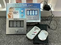 Photo showing the Conair Solarise dawn simulator light therapy and clock alongside the Omron Sport Massager and its carrying pouch on a countertop.