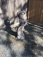 Full view of Diana kneeling statue in outdoor gravel area against wood fence.