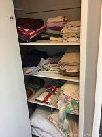 Full view of shelf with stacks of folded linens including towels, sheets, baby blankets, and pillows.