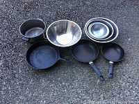 Photo of all pans, bowls, and colander arranged on a pebble surface