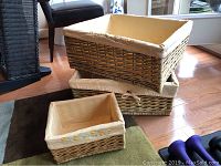 Set of three wicker storage baskets, two large stacked and one small in front, all have beige fabric liners embroidered with flowers.