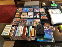 View of DVD movies, books, Wii console and Step device, workout DVDs AND hand weights laid out on table.