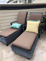 Two grey synthetic wicker chaise lounges with brown cushions and aqua and yellow pillows on balcony