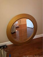 Photo showing the front view of the round beveled mirror with gold frame against a beige wall and hardwood floor.