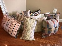 Group of decorative pillows showing variety of patterns and colors on wooden floor against wall