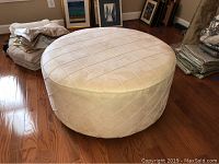 Front and side view of round microfiber hassock ottoman on hardwood floor with quilted diamond pattern upholstery.