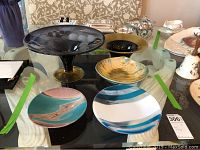 Top view of five painted and glazed art pottery plates and two glass bowls with blue and white stripes on a glass table.