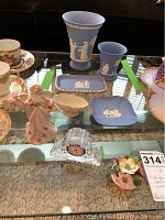 Photo of assorted Wedgwood jasperware pieces, Lenox figurine, porcelain cups, and Coalport flowers on glass table