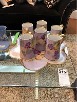 Set of six Limoges porcelain tankards on matching serving tray with grapevine design and gold trim.