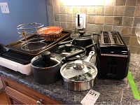 Kitchen counter view of cookware set showing covered pots and pans, copper molds, ham holder, cookie sheets, and electric griddle.