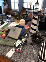 Birch planter with faux greenery, white covered vase, black and white striped lighthouse, blue decorative box, glass bowl, metal spoon, and other decorative items on granite countertop.