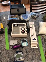 Full lot overview on countertop showing most items including the speaker, weather radio, CD player, digital camera, iPod, selfie stick, and wrist health monitor.