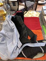 Lot arranged on a table showing woven placemats, two aprons including one denim and one black faux fur lined, and floral napkins.