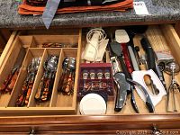 Top view of drawer with Barenthal flatware with faux tortoise handles including knives, forks, and spoons plus kitchen utensils like electric knife, spatulas, measuring spoons, ice cream scoop, wine opener and more.