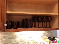 Photo showing the shelf with 8 amber short glasses, 5 amber tall glasses, and 8 amber stemmed wine glasses arranged in a wooden cabinet.