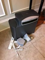 Image showing the entire system including the subwoofer, two satellite speakers, remote control, and cables on tile floor.