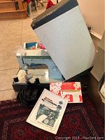Singer sewing machine model 252 with pedal, original manual, and dressmaking book placed on rug and near tiled floor.
