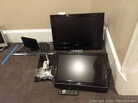 Two flatscreen TVs grouped on carpeted floor, Toshiba larger and LG smaller, both with remotes and stands near them.