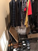Photo showing assorted men's jackets and shirts on hangers above and several pairs of shoes on the floor beneath them.