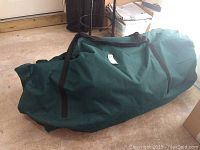 Green canvas carrying bag containing the artificial Christmas tree for compact storage and transport.