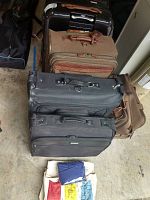 Stack of various luggage bags in black and brown colors, including Hartman, Swisgear, and Tommy Bahama brands.