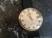 Close-up top view of watch face showing silver dial, gold markers, hands, date window